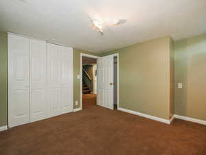 Unfurnished bedroom with a closet, dark carpet, and a textured ceiling