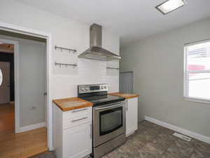 Kitchen featuring stainless steel electric range oven, butcher block counters, extractor fan, and white cabinetry