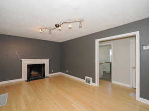 Unfurnished living room with a tiled fireplace, a textured ceiling, and light hardwood / wood-style flooring