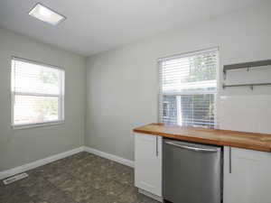 Kitchen featuring stainless steel dishwasher, white cabinets, plenty of natural light, and wooden counters