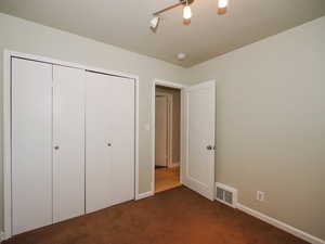 Unfurnished bedroom featuring dark colored carpet, track lighting, and a closet