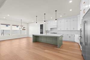 Kitchen featuring white cabinetry, light hardwood / wood-style floors, a center island with sink, decorative backsplash, and decorative light fixtures