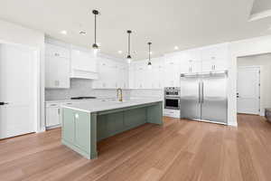 Kitchen featuring tasteful backsplash, light hardwood / wood-style floors, pendant lighting, white cabinetry, and stainless steel appliances