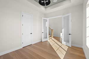 Unfurnished bedroom with light wood-type flooring, french doors, and a tray ceiling