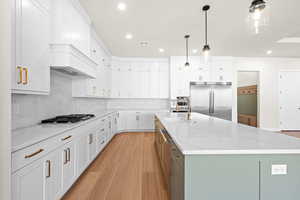 Kitchen with decorative light fixtures, a large island with sink, stainless steel appliances, and white cabinetry