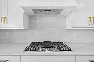 Kitchen featuring stainless steel gas cooktop, white cabinets, tasteful backsplash, and light stone countertops