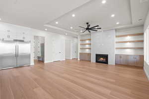 Living room with a premium fireplace, light hardwood / wood-style floors, a tray ceiling, and ceiling fan