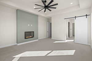 Primary bedroom with light carpet, ceiling fan, a barn door, and a tray ceiling