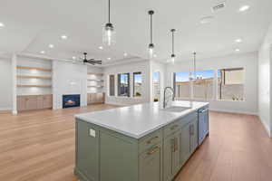 Kitchen featuring ceiling fan with notable chandelier, built in shelves, a fireplace, sink, and a kitchen island with sink