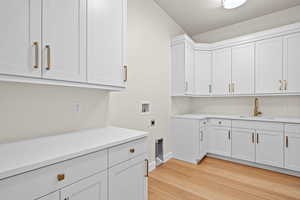 Laundry room with sink, hookup for a washing machine, light wood-type flooring, hookup for an electric dryer, and cabinets