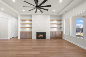 Living room featuring ceiling fan, built in features, a premium fireplace, and light hardwood / wood-style flooring