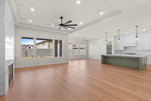 Living room with ceiling fan, a raised ceiling, a tile fireplace, and light hardwood / wood-style floors