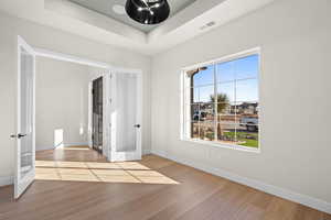 Bedroom featuring wood-type flooring, a tray ceiling, and french doors