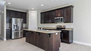 Kitchen featuring a center island with sink, stainless steel appliances, dark brown cabinets, a breakfast bar, and sink