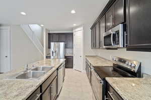 Kitchen featuring sink, dark brown cabinetry, light stone countertops, appliances with stainless steel finishes, and light tile patterned floors