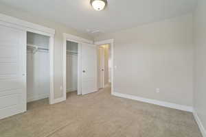 Unfurnished bedroom with light colored carpet and two closets