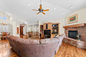 Living room with lofted ceiling, dark wood-type flooring, ceiling fan with notable chandelier, and a stone fireplace