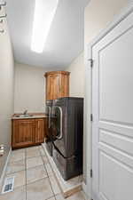 Laundry area featuring light tile patterned floors, a textured ceiling, washing machine and dryer, cabinets, and sink