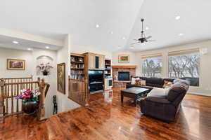 Living room featuring ceiling fan, vaulted ceiling, a fireplace, and dark hardwood / wood-style flooring