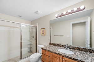 Bathroom with toilet, a shower with shower door, and vanity