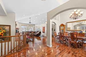 Dining area with ceiling fan with notable chandelier, a towering ceiling, hardwood / wood-style flooring, and a stone fireplace