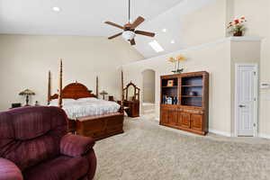 Bedroom featuring ceiling fan, light colored carpet, ensuite bathroom, a skylight, and high vaulted ceiling