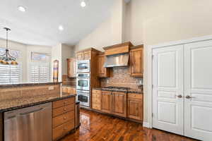 Kitchen featuring exhaust hood, stainless steel appliances, tasteful backsplash, lofted ceiling, and pendant lighting