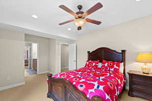 Bedroom featuring ensuite bath, ceiling fan, and light carpet