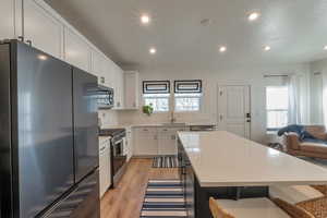 Kitchen featuring white cabinets, a kitchen bar, stainless steel appliances, and a center island