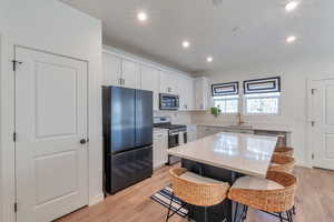 Kitchen with appliances with stainless steel finishes, a kitchen island, white cabinetry, sink, and a breakfast bar