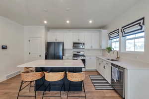 Kitchen featuring light hardwood / wood-style floors, appliances with stainless steel finishes, a kitchen island, white cabinets, and sink