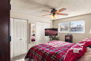 Carpeted bedroom featuring a textured ceiling, ceiling fan, and multiple closets