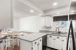 Kitchen featuring sink, white cabinets, black dishwasher, and kitchen peninsula