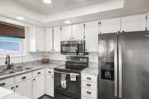 Kitchen featuring stainless steel appliances, white cabinetry, light stone counters, and sink