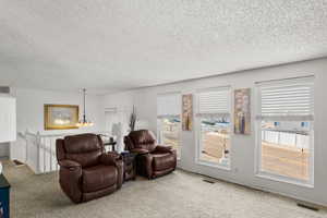 Living room with a textured ceiling, an inviting chandelier, a wealth of natural light, and carpet floors