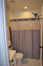 Bathroom with toilet, a shower with shower curtain, tile patterned flooring, and vanity