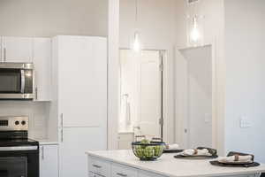 Kitchen featuring light stone countertops, white cabinets, hanging light fixtures, and appliances with stainless steel finishes