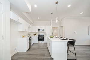 Kitchen with hardwood / wood-style floors, a kitchen bar, white cabinetry, stainless steel appliances, and hanging light fixtures