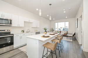 Kitchen with light hardwood / wood-style floors, hanging light fixtures, a breakfast bar area, stainless steel appliances, and white cabinets