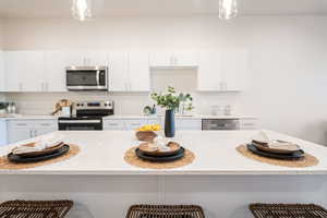 Kitchen featuring stainless steel appliances, pendant lighting, white cabinetry, and a breakfast bar