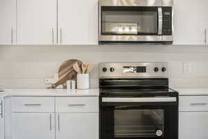 Kitchen with appliances with stainless steel finishes, white cabinets, and light stone counters