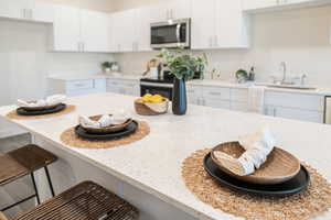 Kitchen with a kitchen bar, sink, white cabinetry, and light stone countertops