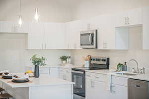 Kitchen with stainless steel appliances, white cabinetry, and hanging light fixtures