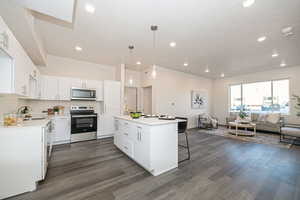 Kitchen with a kitchen island, hanging light fixtures, stainless steel appliances, white cabinets, and dark hardwood / wood-style flooring