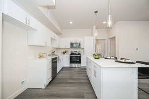 Kitchen featuring a breakfast bar area, appliances with stainless steel finishes, pendant lighting, white cabinets, and sink