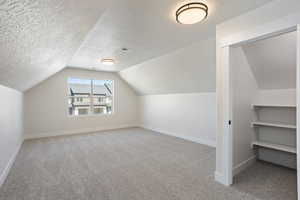 Bonus room featuring a textured ceiling, vaulted ceiling, and light colored carpet