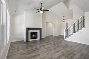 Unfurnished living room with a brick fireplace, a wealth of natural light, ceiling fan with notable chandelier, and hardwood / wood-style flooring