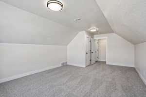 Additional living space featuring light carpet, vaulted ceiling, and a textured ceiling