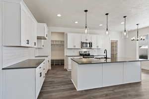 Kitchen with a center island with sink, sink, hanging light fixtures, appliances with stainless steel finishes, and white cabinets