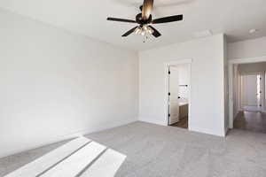 Unfurnished bedroom featuring ceiling fan, ensuite bathroom, and carpet floors